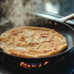 a golden-brown cottage cheese flatbread cooking in a nonstick pan on a stove